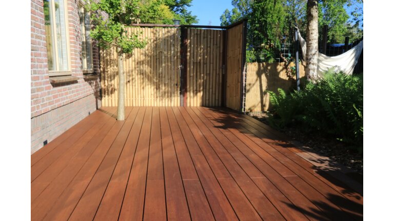 Holzterrasse mit Bambuszaun und Baum.
